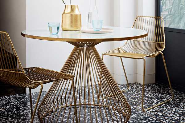 Round brass dining table with two brass wire dining chairs.